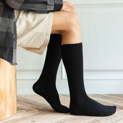 Mann trägt schwarze Kniestrümpfe aus Baumwolle, sitzt auf Holzbank, beige Shorts.