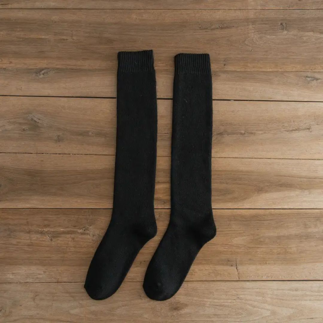 Schwarze Kniestrümpfe aus Baumwolle auf Holzboden, bequeme Damenmode, warme Socken.