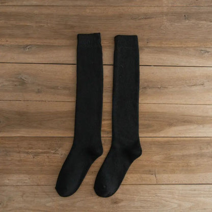 Schwarze Kniestrümpfe aus Baumwolle auf Holzboden, bequeme Damenmode, warme Socken.
