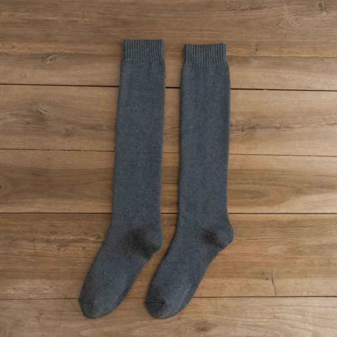 Graue Kniestrümpfe aus Wolle auf Holzboden, warme Winterstrümpfe, gemütliche Socken.