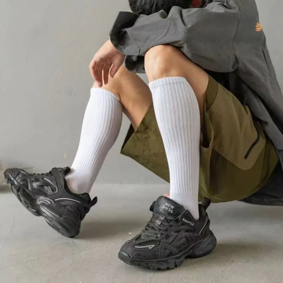 Schwarze Sneaker, sportlich, Herrenmode, knielange weiße Socken, olivgrüne Shorts, graue Jacke.