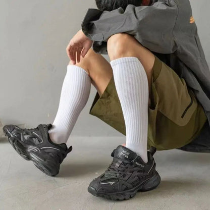 Schwarze Sneaker, sportlich, Herrenmode, knielange weiße Socken, olivgrüne Shorts, graue Jacke.