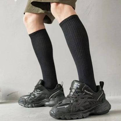 Schwarze Sportschuhe mit dicken Sohlen, schwarze Kniestrümpfe, grauer Hintergrund.