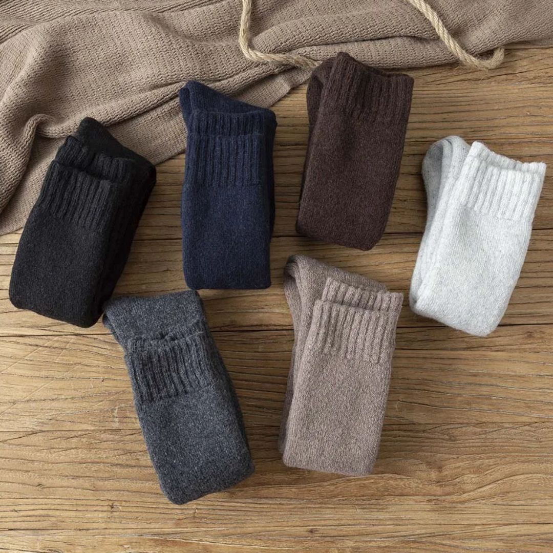 Sechs Paar Wollsocken in verschiedenen Farben auf Holztisch, warme Winterkleidung.