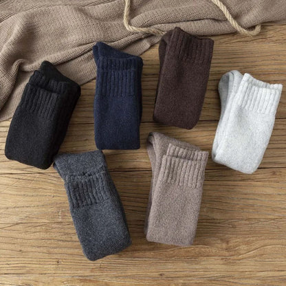 Sechs Paar Wollsocken in verschiedenen Farben auf Holztisch, warme Winterkleidung.