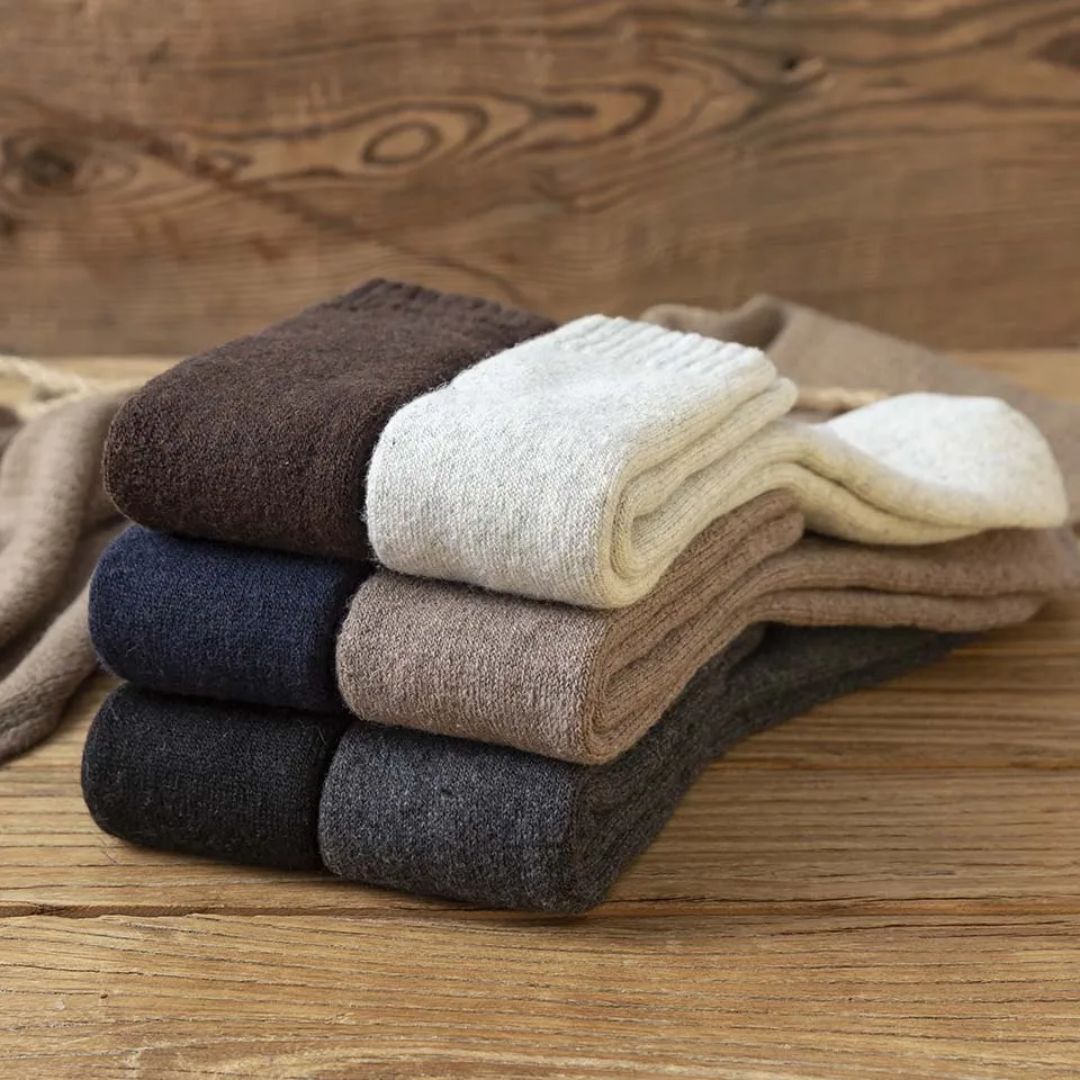 Vier Paar Wollsocken in Braun, Creme, Blau und Grau auf Holzuntergrund, warme Winterkleidung.