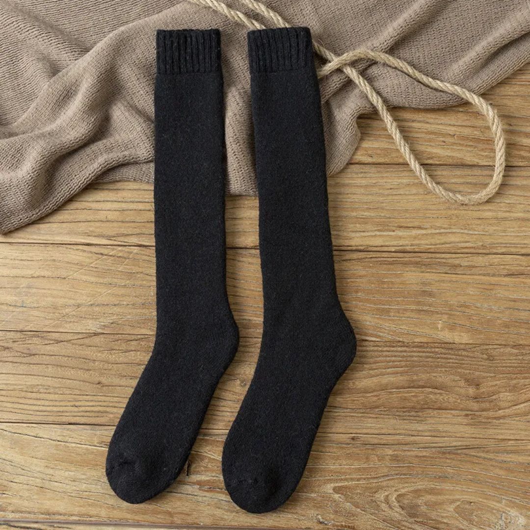 Schwarze Kniestrümpfe aus Baumwolle auf Holzboden, ideal für Herbstmode.