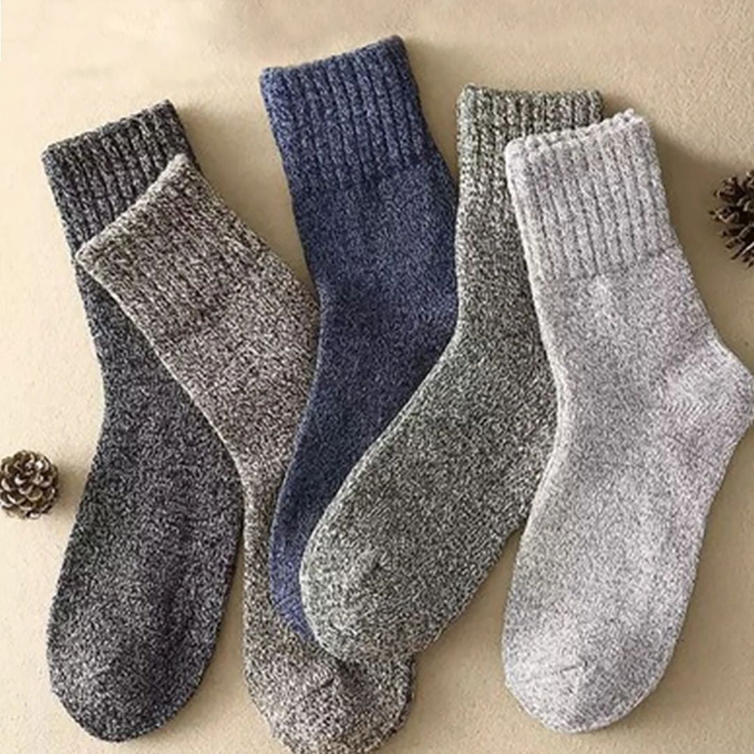 Vier Paar warme Wollsocken in Grau und Blau auf beigem Hintergrund, ideal für den Winter.