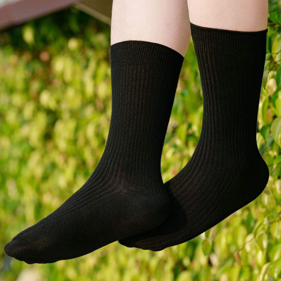 Schwarze Baumwollsocken, knöchelhoch, unisex, vor grünem Hintergrund, bequem und atmungsaktiv.