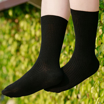 Schwarze Baumwollsocken, knöchelhoch, unisex, vor grünem Hintergrund, bequem und atmungsaktiv.