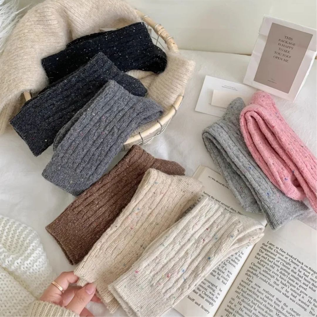 Verschiedene gestrickte Wollschals in Beige, Grau, Rosa und Schwarz auf einem Tisch.