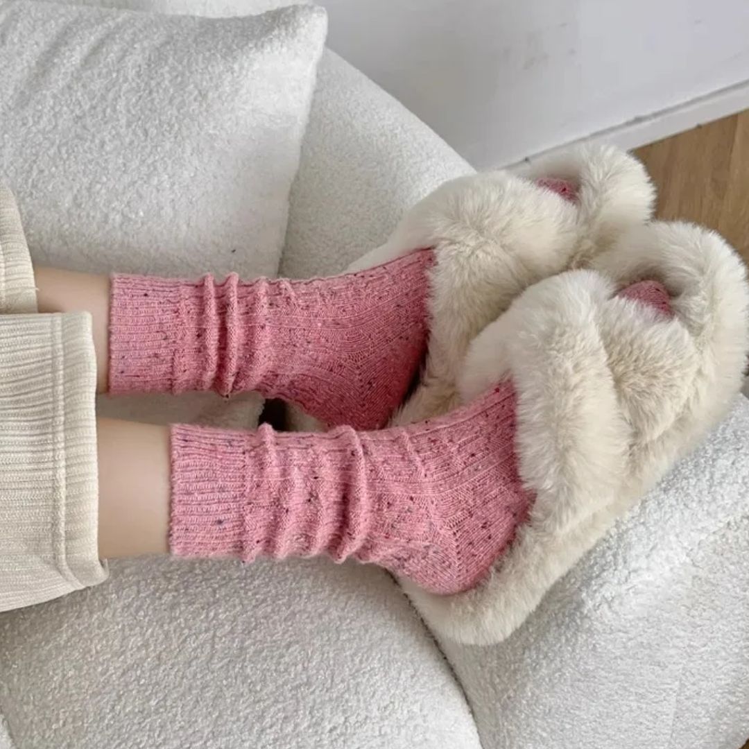 Rosa Socken und flauschige Hausschuhe auf weißem Sofa, gemütliche Wintermode.