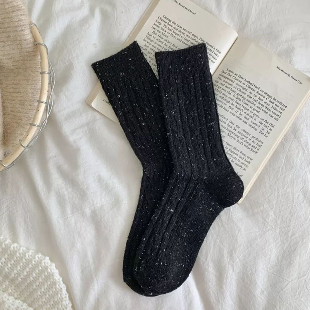 Schwarze Stricksocken auf offenem Buch, gemütliches Design, warme Winterkleidung.