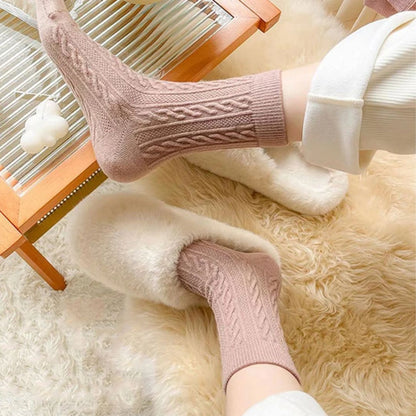 Rosa Stricksocken und flauschige Hausschuhe auf Teppich, gemütliche Wintermode.
