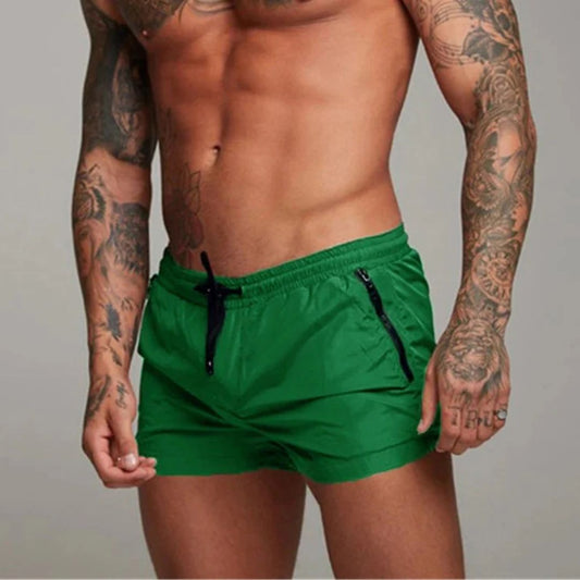 Mann in grüner Badehose, tätowierte Arme, muskulöser Oberkörper, sportliche Herrenmode.