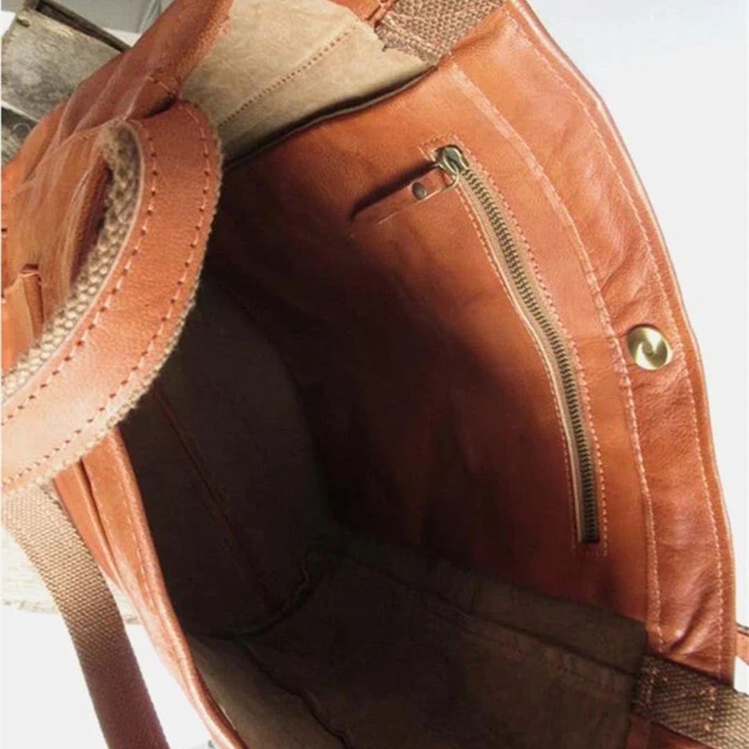 Innenansicht einer braunen Ledertasche mit Reißverschlussfach und Druckknopfverschluss.