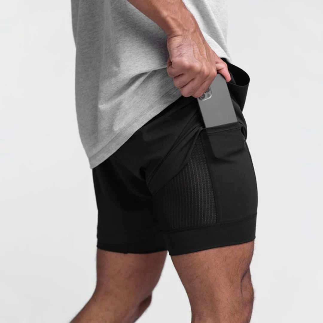Mann in schwarzer Sportshorts mit Smartphone in der Tasche, Fitnessbekleidung, Herrenmode.