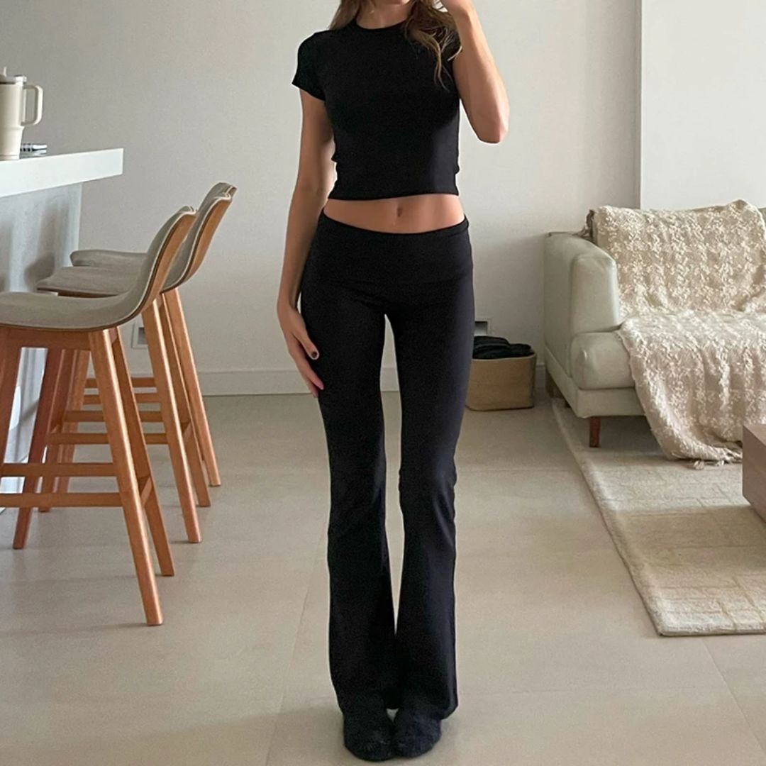 Frau in schwarzem Crop-Top und Schlaghose in modernem Wohnzimmer.