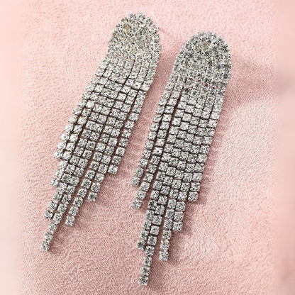 Silberne Strass-Ohrringe mit langen Fransen auf rosa Hintergrund, glamouröser Schmuck.