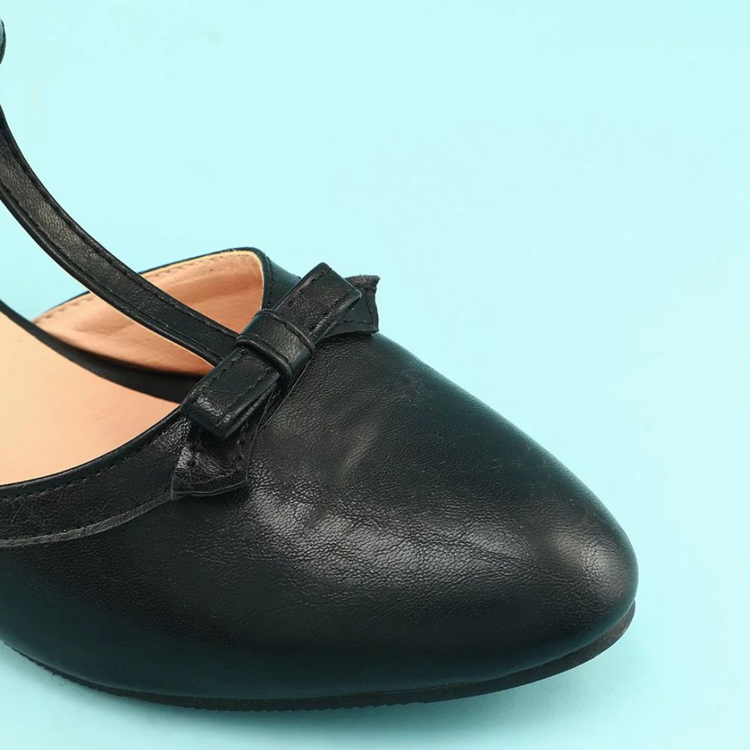 Schwarzer Damen-Ballerina-Schuh mit Schleife, Lederoptik, auf hellblauem Hintergrund.