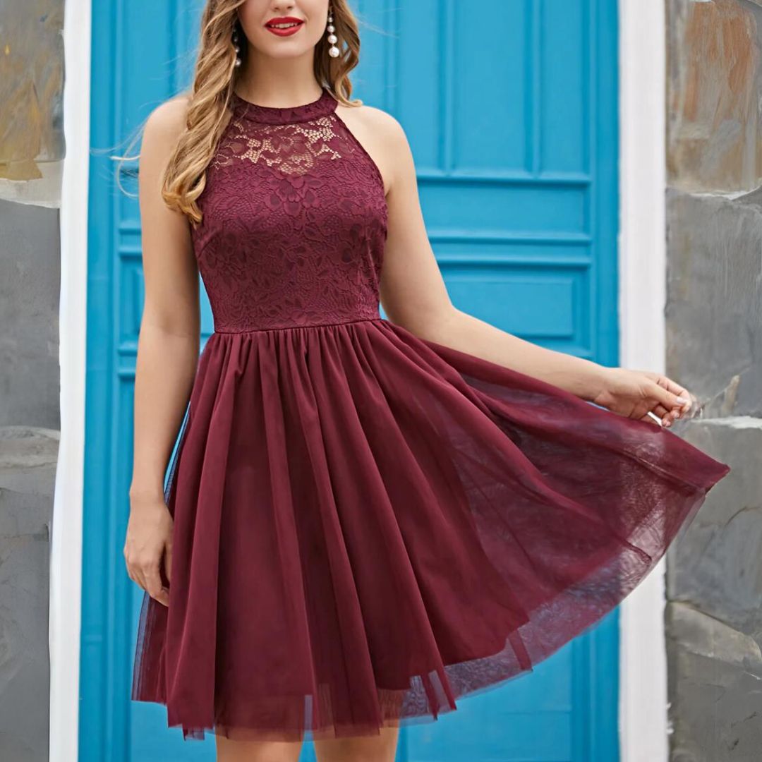 Frau in burgunderrotem Spitzenkleid vor blauer Tür, elegantes Abendkleid, ärmellos.