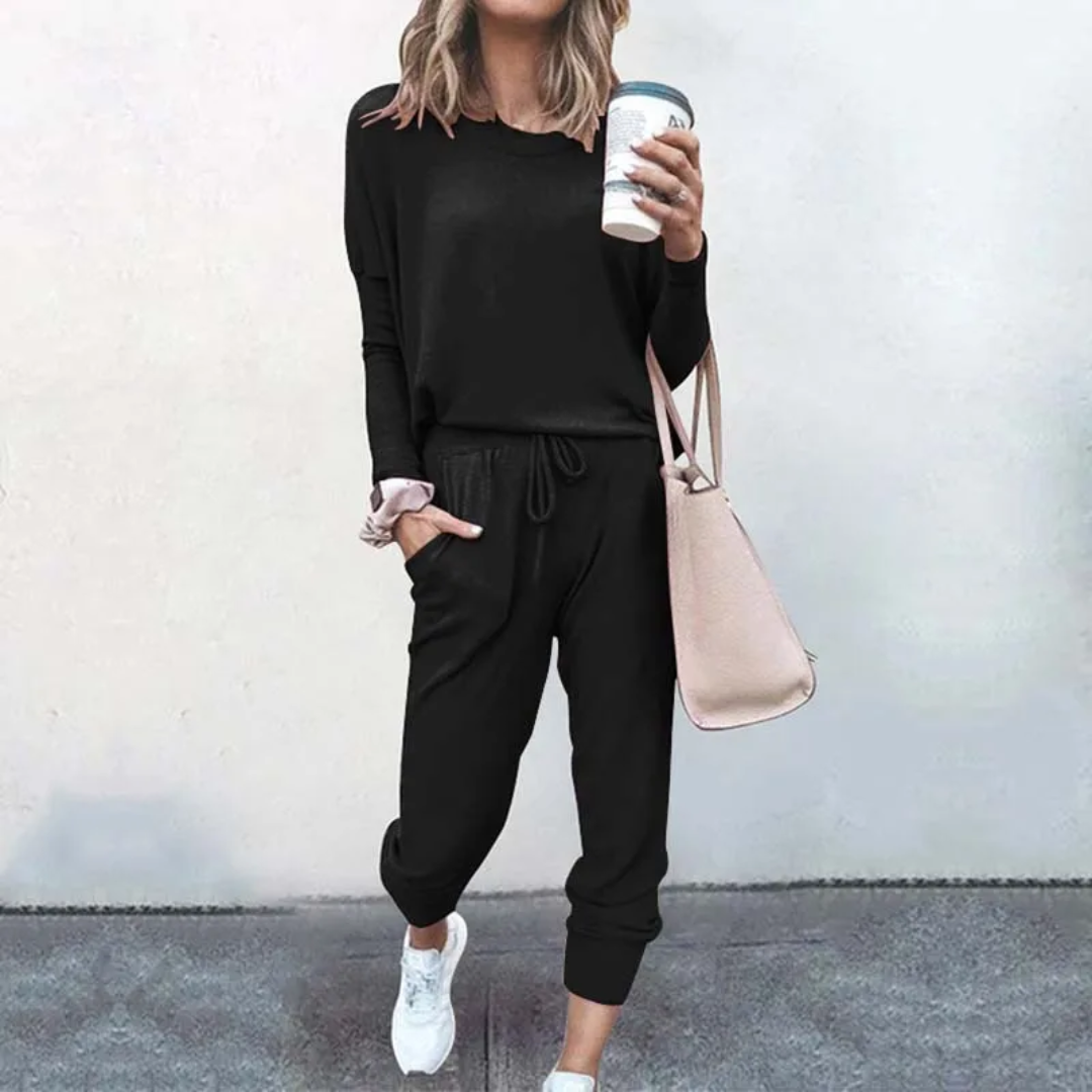 Frau in schwarzem Jogginganzug mit Kaffeebecher und rosa Tasche, lässige Mode.