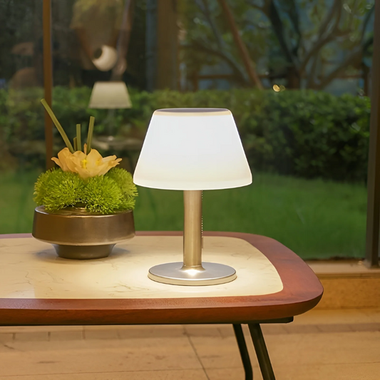 Moderne Tischlampe aus Metall mit weißem Schirm auf Holztisch, dekorative Beleuchtung.