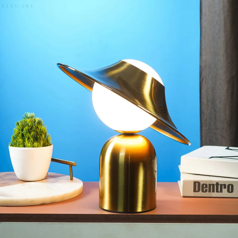 Moderne Tischlampe aus Metall, goldfarben, mit rundem Schirm, auf Holztisch vor blauem Hintergrund.