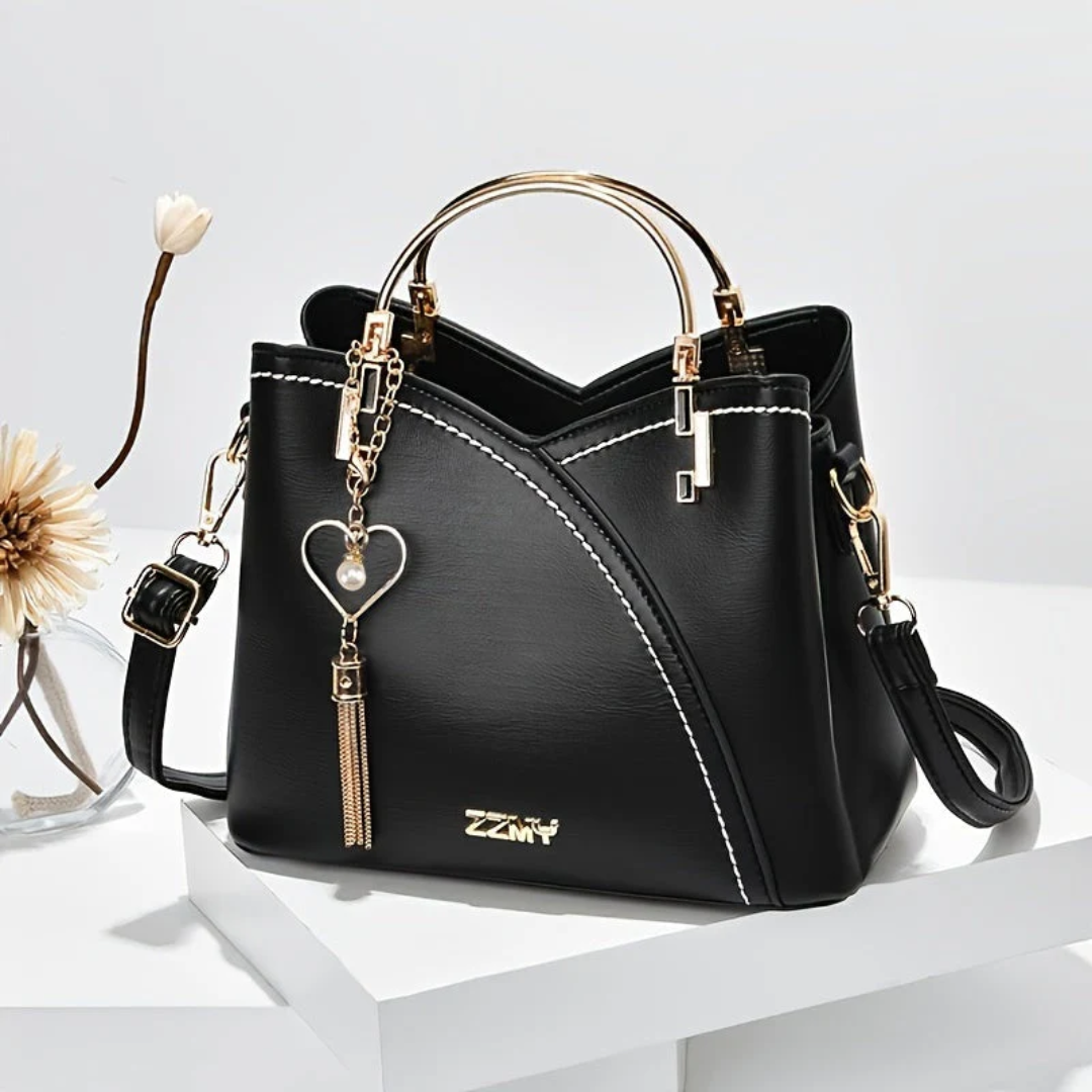 Schwarze Damenhandtasche aus Leder mit goldenen Griffen und Herzanhänger, elegant und modern.