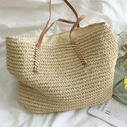 Beiger Strohtasche mit braunen Ledergriffen auf weißem Hintergrund, ideal für Sommer und Strand.