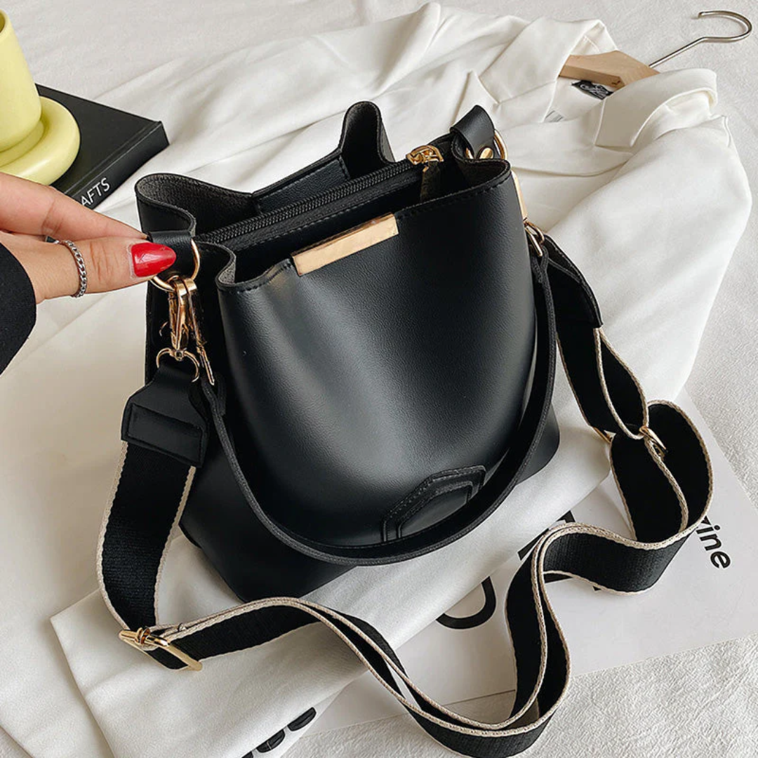 Schwarze Lederhandtasche mit goldenen Details und verstellbarem Schultergurt auf weißem Hintergrund.