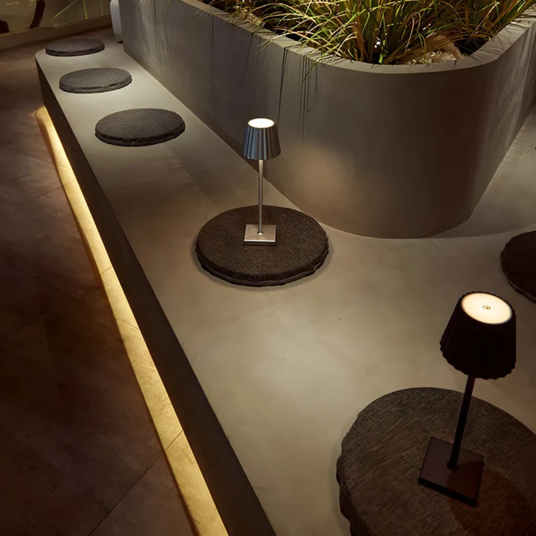 Moderne Tischlampen auf Betonbank mit runden Sitzkissen, stilvolle Innenbeleuchtung.