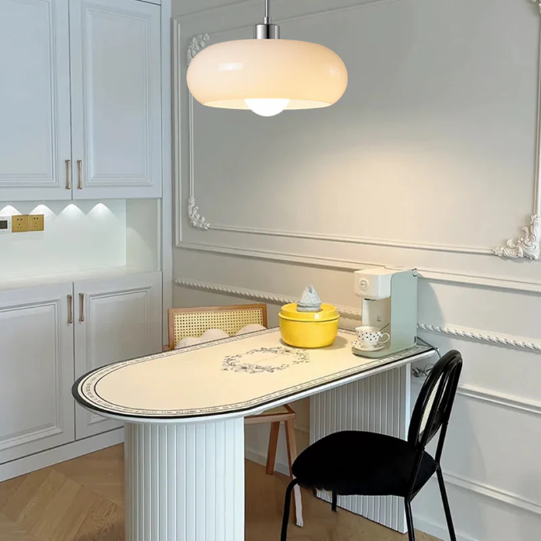 Moderne Küche mit weißem Tisch, gelber Schüssel, schwarzem Stuhl und eleganter Hängelampe.