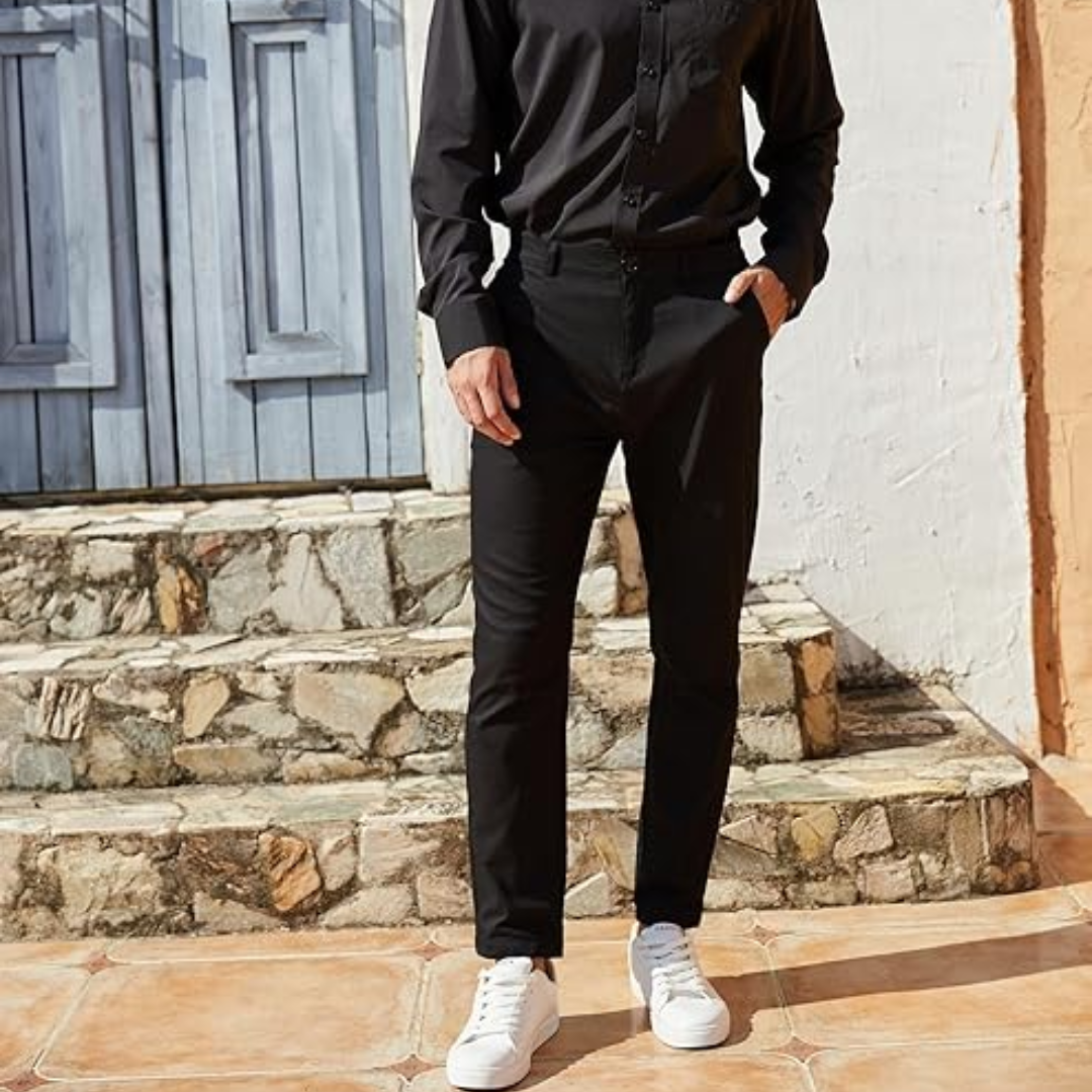 Mann in schwarzem Hemd und Hose, weiße Sneaker, steht vor blauer Holztür, modisch, lässig.
