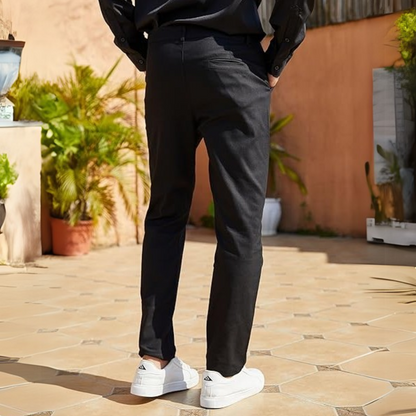 Mann in schwarzer Hose und weißen Sneakers im Freien, modische Freizeitkleidung, Terrakotta-Hintergrund.