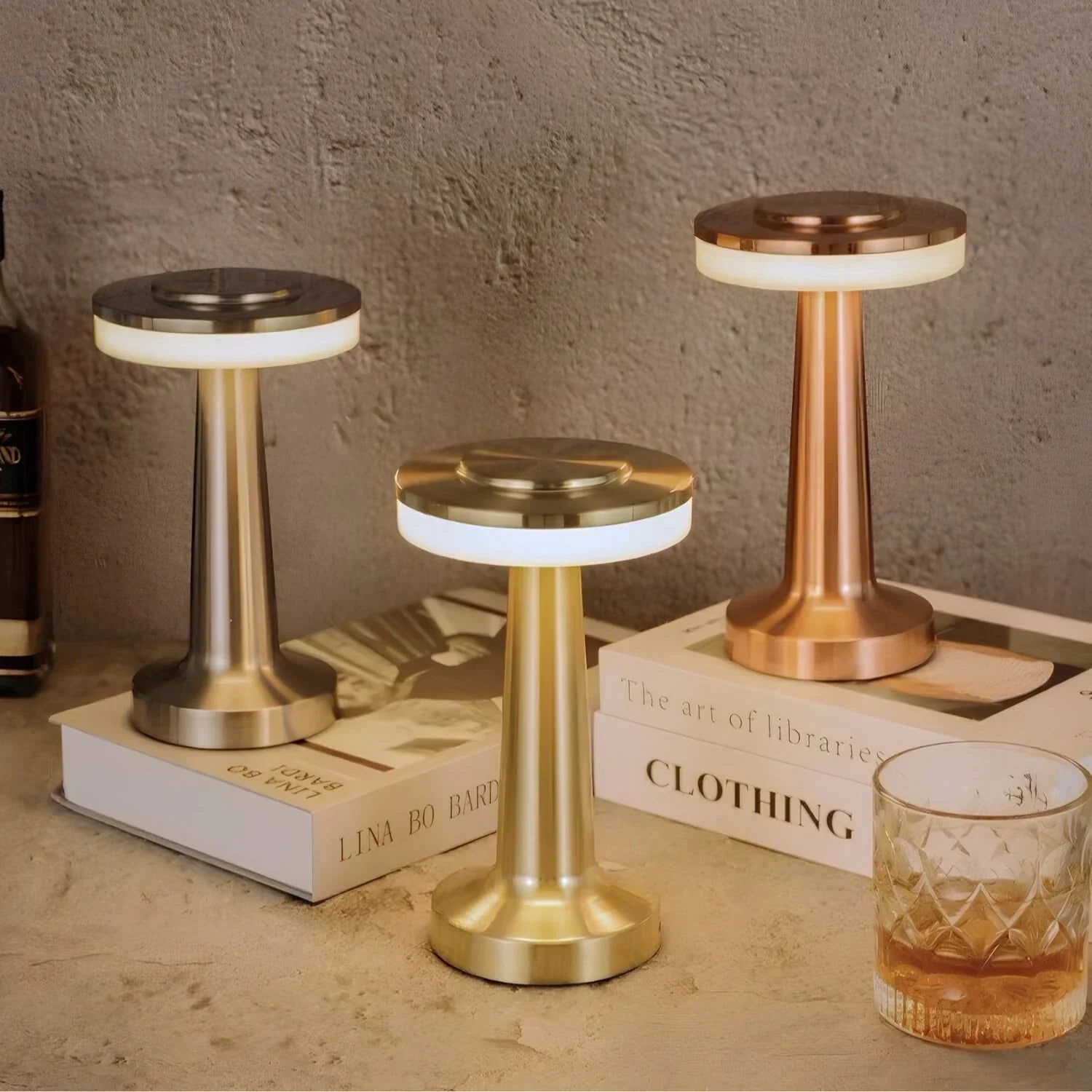 Drei LED-Tischlampen aus Metall in Gold, Silber und Kupfer auf Büchern, modernes Design.