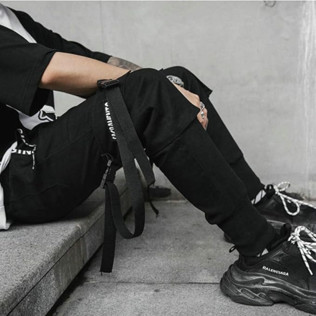 Mann in schwarzer Streetwear-Hose mit Gurt und schwarzen Sneakers, urbaner Stil.