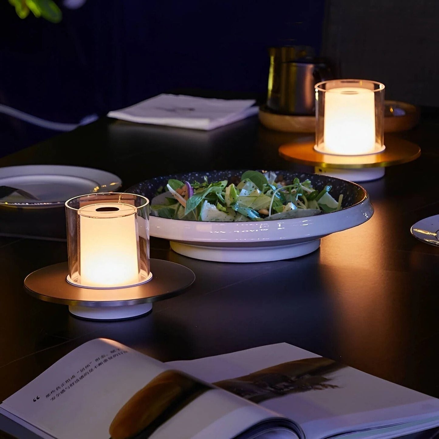 Moderne LED-Tischlampe, warmweiß, zylindrisch, auf Esstisch neben Salatteller, Abendessen.