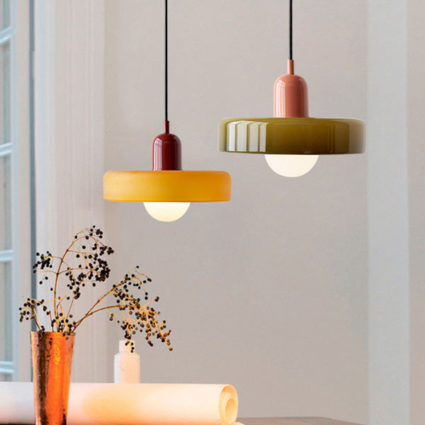 Zwei moderne Hängelampen, gelb und olivgrün, aus Glas über einem Tisch mit Dekoration.