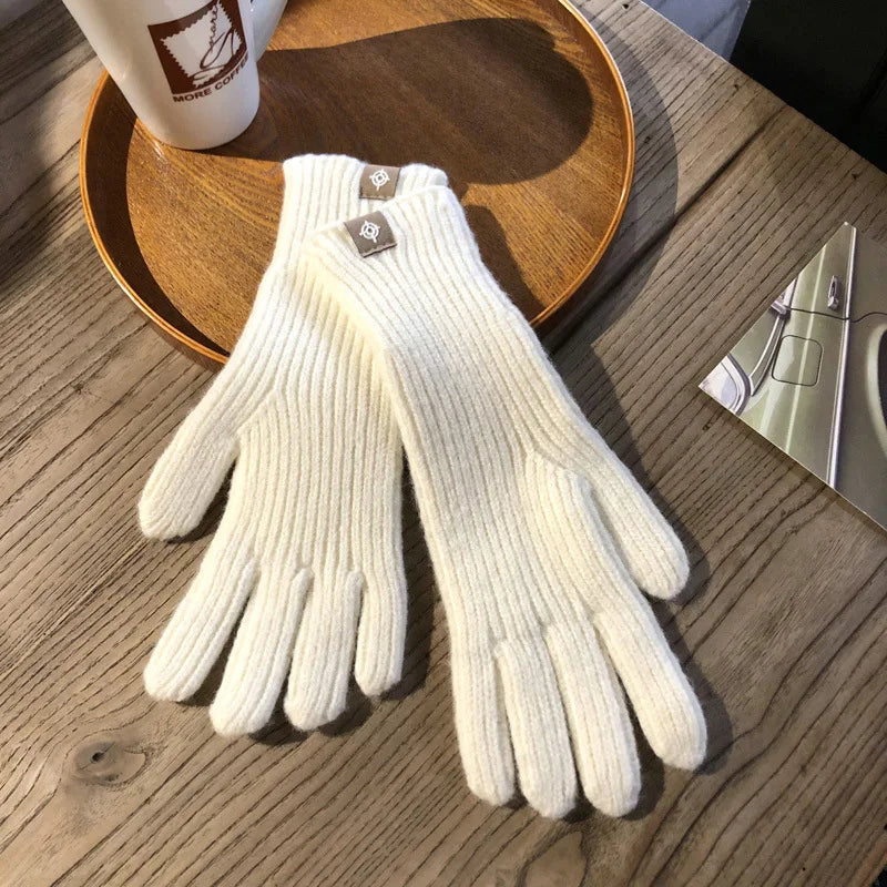 Weiße Strickhandschuhe aus Wolle auf Holztisch, ideal für Wintermode und kaltes Wetter.