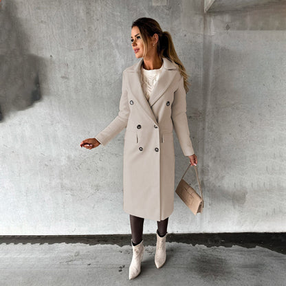 Frau in beigem Wintermantel, Doppelreiher, weiße Stiefel, Handtasche, Betonhintergrund.