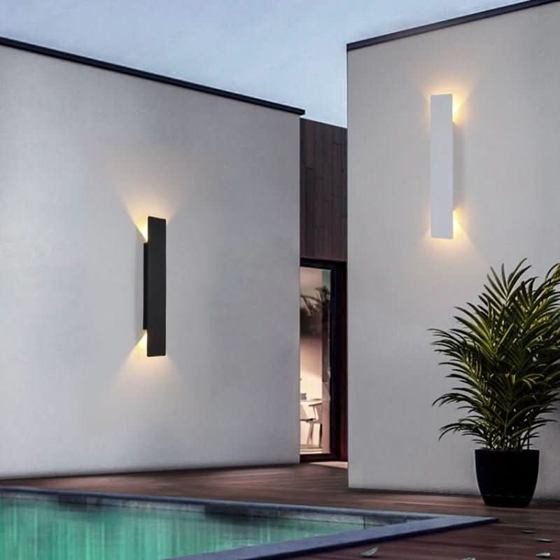 En svart och en vit vägglampa på vita väggar vid en pool, med en kruka med palm intill. 4