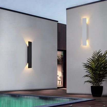 En svart och en vit vägglampa på vita väggar vid en pool, med en kruka med palm intill. 4