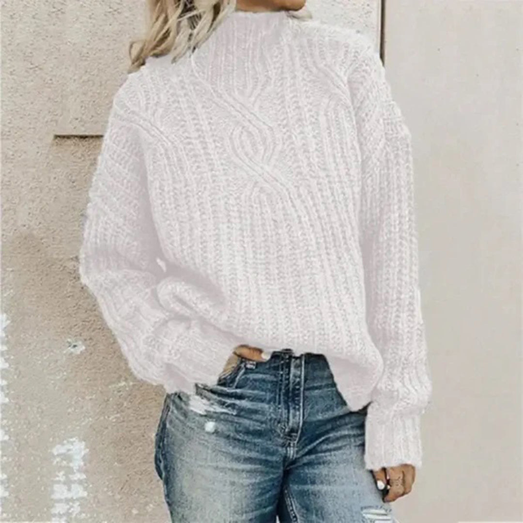Frau in weißem Strickpullover und blauer Jeans vor beiger Wand.