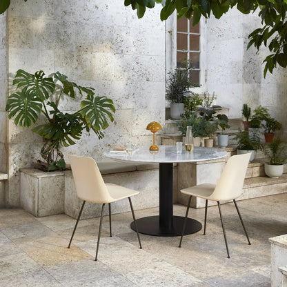 Moderner Garten mit Marmortisch, zwei weißen Stühlen, gelber Lampe, Pflanzen, Steinwand.