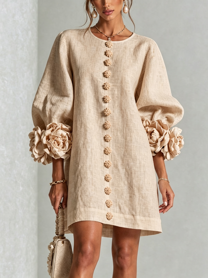 Beige miniklänning framifrån på modell i studio, med rad av blommiga knappar och stora blommanschetter på puffärmarna. 23