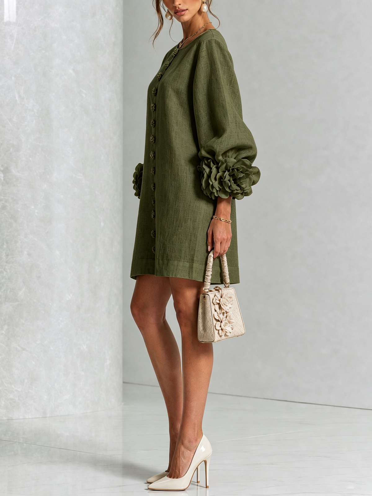 Olivgrön miniklänning i sidovy, modellen med liten beige väska och vita pumps, rosmanschetten syns på ärmen. 8