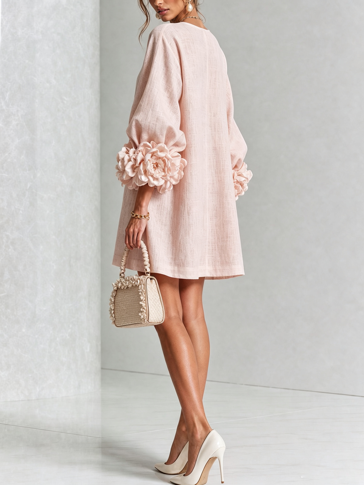 Rosa miniklänning sedd bakifrån och från sidan på modell med stora blommande manschetter, vit högklackad sko och beige handväska. 21
