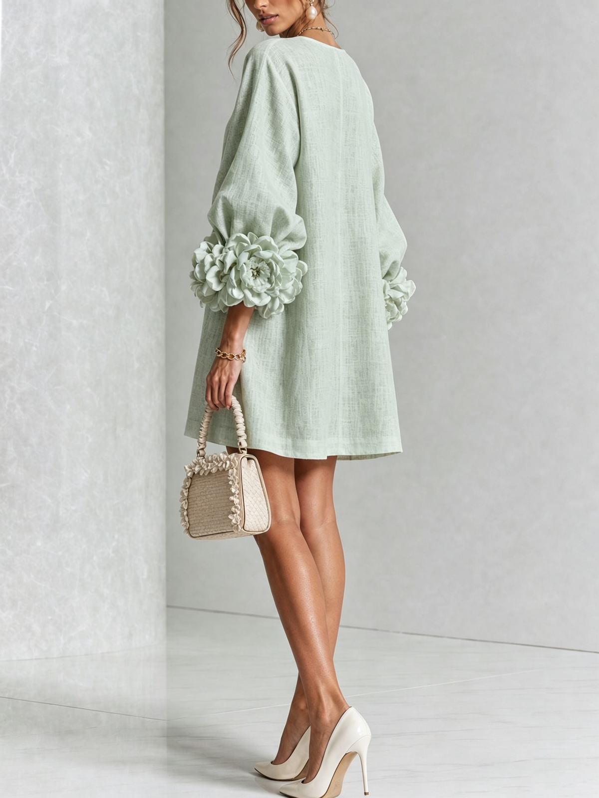 Ljusgrön miniklänning bakifrån på modell med stora blommanschetter, beige handväska och vita högklackade skor. 33
