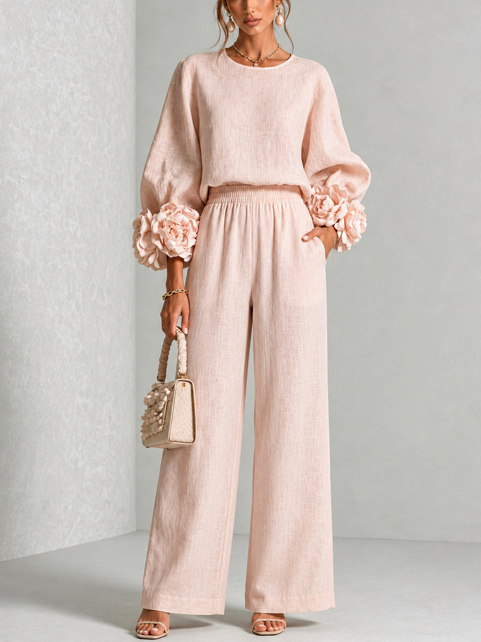 Modell i rosa set med ballongärmar, blomdetaljer och vida byxor, framifrån med handväska 1